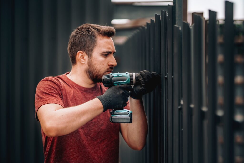 Caucasian construction man working with screwdriver on metal fence