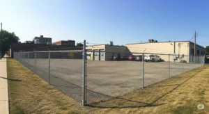 A wide-angle shot of a recently installed commercial chain-link fence surrounding a vibrant commercial property in Buffalo, NY. The image showcases the fence's durability and functionality, with a focus on its ability to provide security and define property lines. The background features a variety of commercial buildings in Buffalo's industrial district, highlighting the diversity of clients who benefit from quality commercial fencing. The lighting in this high-quality photograph is well-balanced, showcasing the fence and its surroundings with clarity and a professional aesthetic. It's a suitable image for a blog post that addresses frequently asked questions about commercial fencing in Buffalo, aiming to convey security, practicality and professionalism.