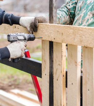 Two men in work clothes are building a fence for their house