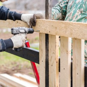 Two men in work clothes are building a fence for their house